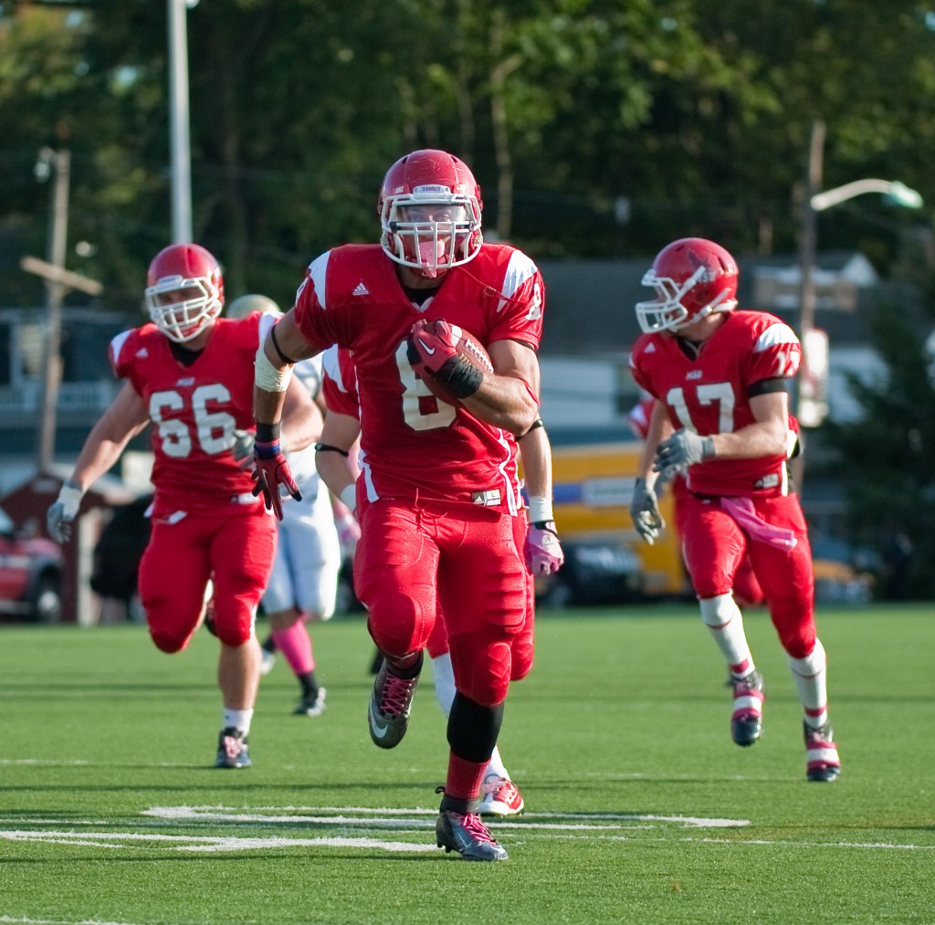 Montclair State University football player returns a punt for a touch down guarded by two players. 2012